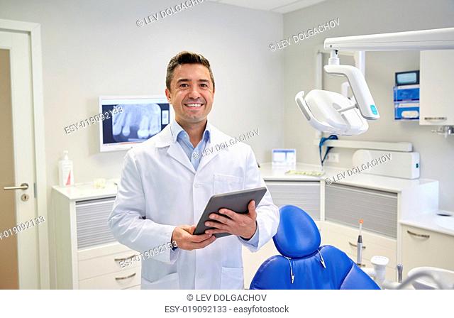 people, medicine, stomatology and healthcare concept - happy middle aged male dentist in white coat with tablet pc computer at dental clinic office