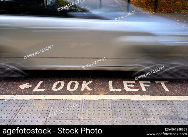 Look Left warning for the careless pedestrians at the pedestrian crosswalk with the moving car in the background in the streets of London, United Kingdom