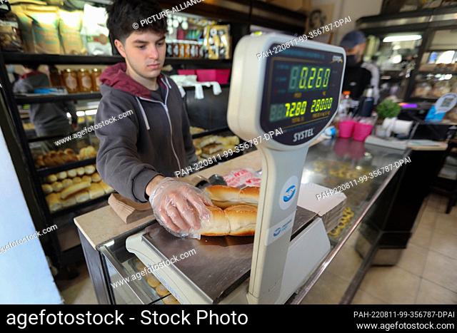 10 August 2022, Argentina, Buenos Aires: A young salesman weighs buns in a store. Prices climbed 71 percent in July compared to the previous year