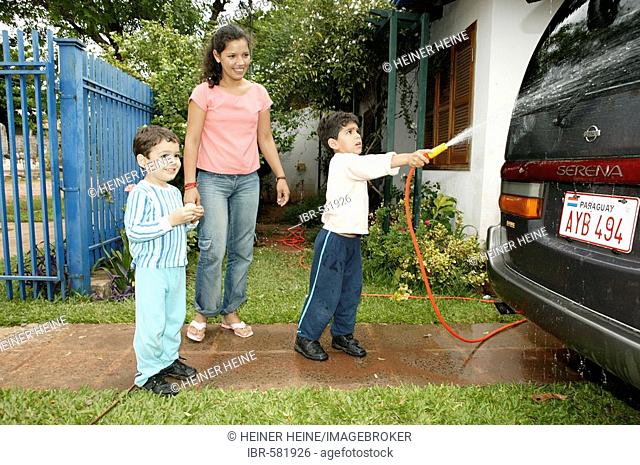 Woman and children washing car with garden hose, Asuncion, Paraguay, South America