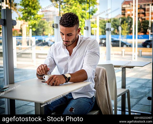 Attractive Man Drinking Coffee while Sitting in a Bar at the Table, with Serious Expression