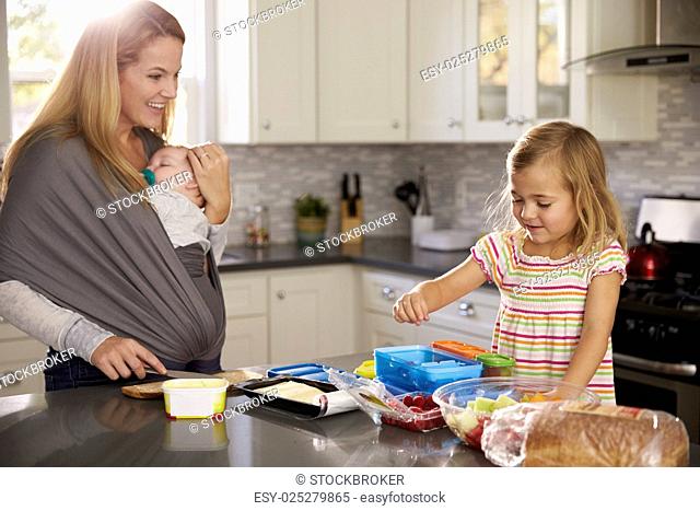 Mum holding baby watches older daughter preparing food