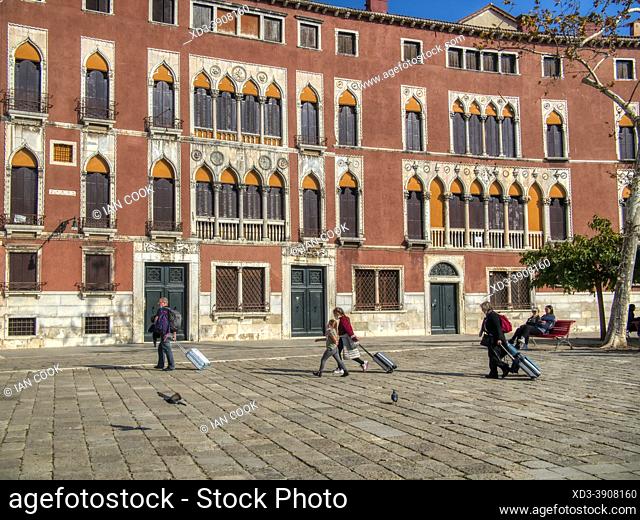 family walkig with rolling suitcases in Campo San Polo, Venice, Italy