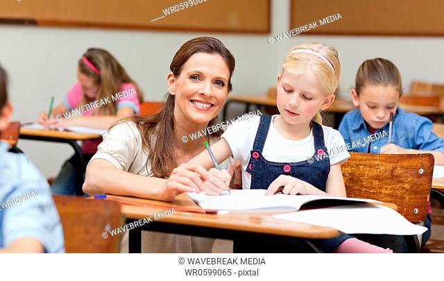 Smiling primary teacher helping student
