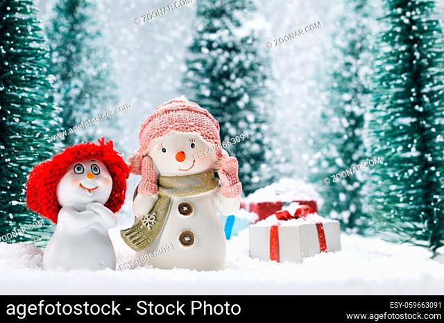 Two small cute snowmen friends with gifts in forest under falling snow