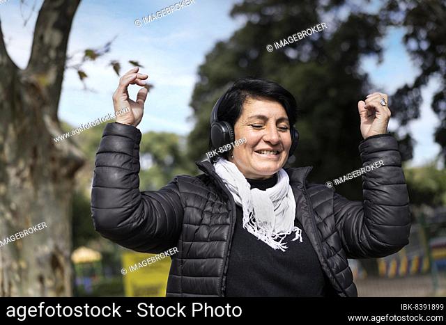 Latin woman listening to music outdoors with headphones. Expression of happiness, winning attitude. Copy space