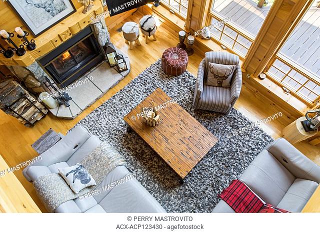 Top view of taupe leather sofas, grey and white striped cloth armchair, distressed wood top coffee table and New Zealand wool rug in living room with riverstone...