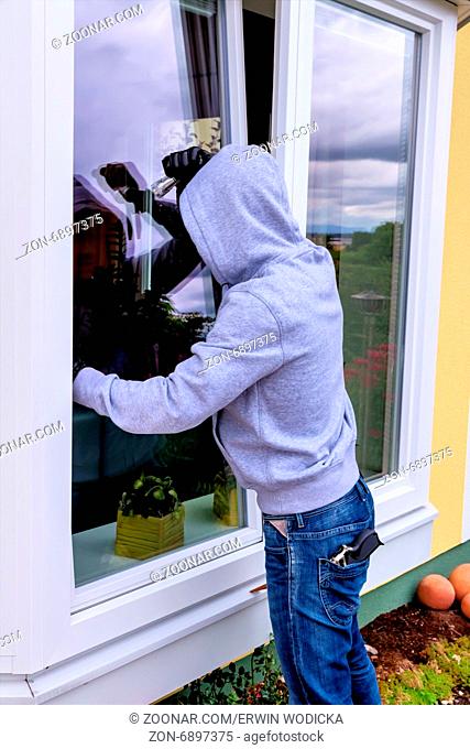 Ein Einbrecher versucht bei einem offenen Fenster mit einer Brechstange einzubrechen