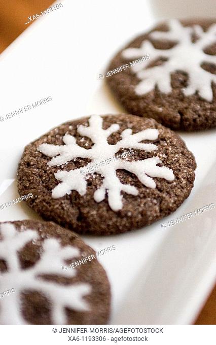 A row of decorated home baked chocolate cookies with white sugary snowflakes piped on in icing