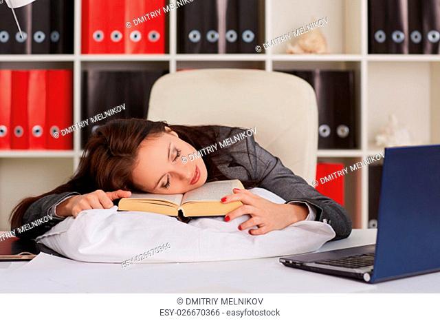 Tired young business woman is sleeping on workplace in the office