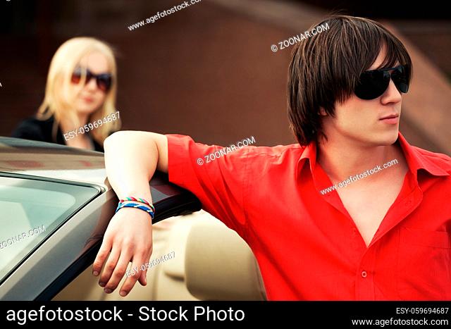 Young handsome fashion man in sunglasses standing by his convertible car