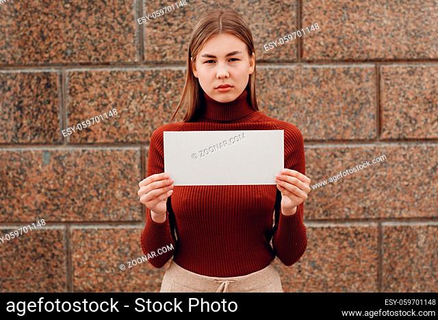 Young woman holds white paper in hand stone background. Young woman with white blank template sheet with empty space