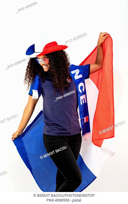 Portrait of a young supporter of the French football team wearing a hat, tricolor glasses and a flag of his team