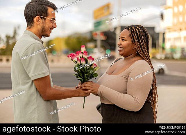 Young man giving bouquet of flowers to girlfriend at footpath