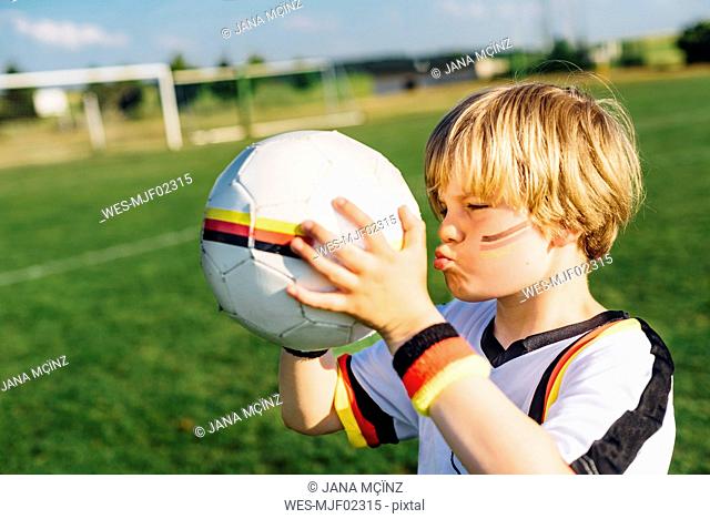 Boy with face paint and German football shirt, kissing soccer ball