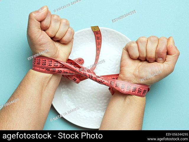 two female hands tied with red measuring tape on a white round ceramic plate, slimming concept, top view