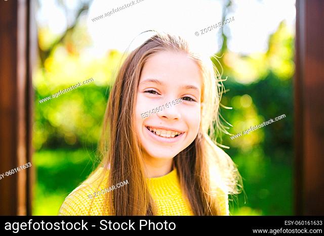 Portrait of modern happy teen girl with dental braces dressed in yellow clothes in park. Pretty teenage girl wearing braces smiling cheerfully