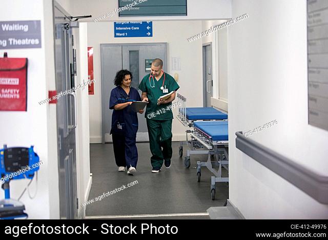 Doctor and surgeon discussing medical chart, walking in hospital corridor