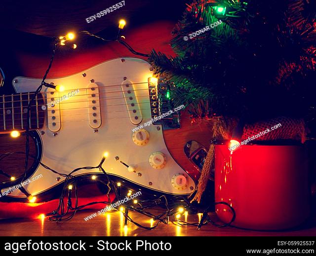 Old used vintage guitar with Christmas lights on a wooden table and space for text