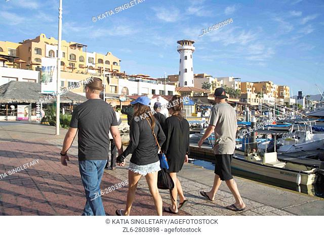 Caucasian Tourists with hats holding hands and touring, having fun, walking in the marina of Cabos San Lucas in Mexico