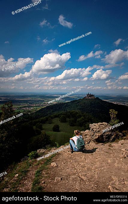 Female explorer admiring view of Burg Hohenzollern Castle while sitting on mountain at Swabian Alb, Germany