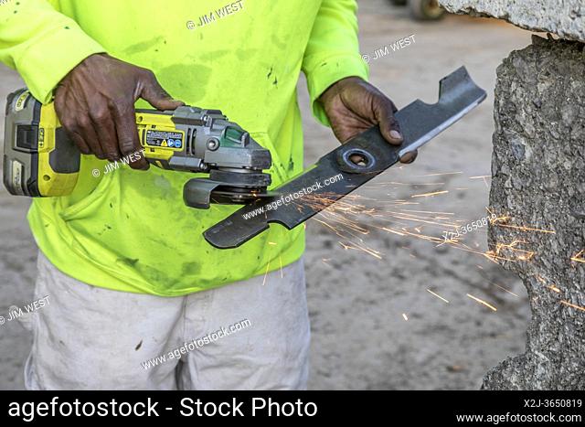 Detroit, Michigan - A worker from the Detroit Grounds Crew sharpens a mower blade before his crew cuts the grass on the grounds of a closed public school