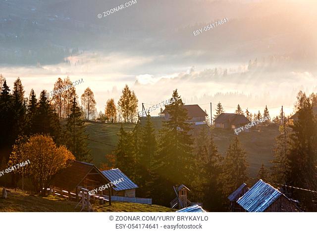 First sunrise rays of sun and shadows through fog and trees on slopes. Morning autumn Carpathian Mountains landscape. Some lens flare effect big blink from sun...