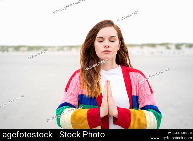 Woman wearing multi colored cardigan sweater standing with hands clasped at beach