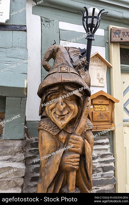 24 May 2021, Saxony-Anhalt, Stolberg: A wooden witch stands in front of a historic half-timbered house in the old town of Stolberg