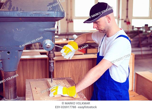 worker with dark cap in a carpenter's workshop using drilling machine