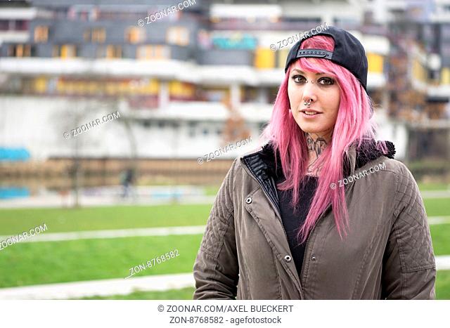 young alternative woman with pink hair standing in front of run-down housing estate