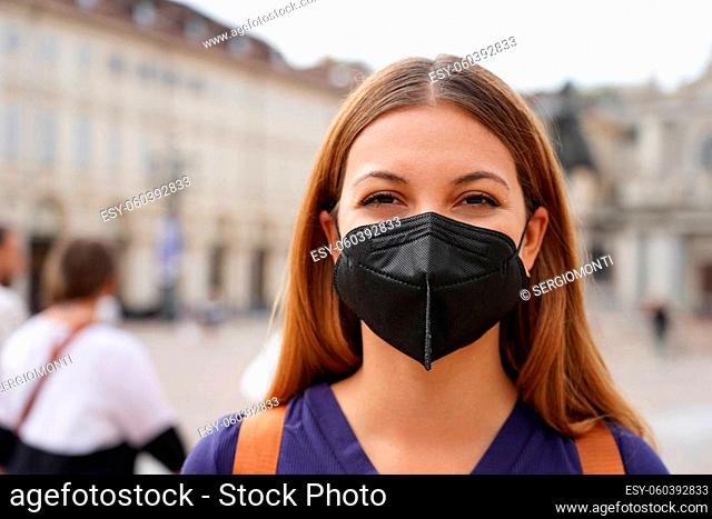 Portrait of student girl wearing a protective KN95 FFP2 black mask looking at camera with urban background