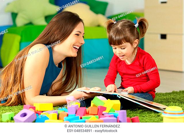 Mother and toddler playing together with a book lying on the floor in the bedroom at home with a colorful background