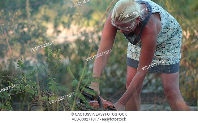 Woman with chainsaw cutting the trunk in forest