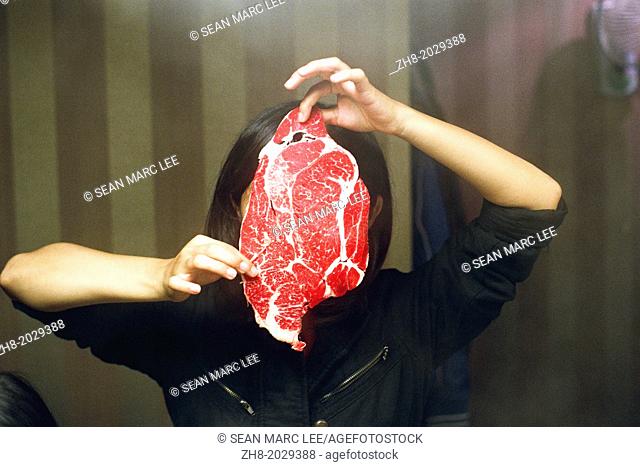 A girl holds a piece of raw beef in front of her face