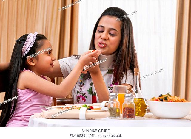 Little girl feeding her mother piece of pizza at restaurant