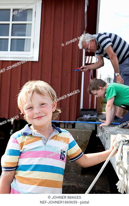 Boy looking at camera, in background brother and grandfather catching crabs