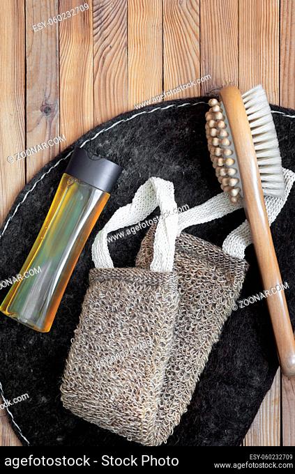 Accessories for visiting a bath or sauna on a wooden background: a washcloth, a mat, a massage brush and shower gel. Top view with copy space