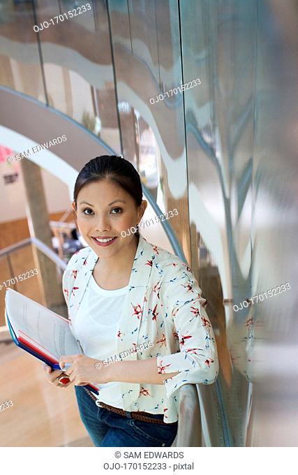 Portrait of smiling businesswoman with paperwork on stairs in office