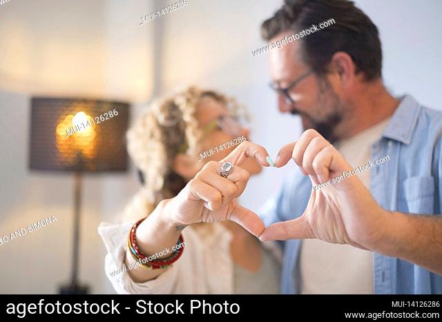 cheerful couple embracing while doing heart shape gesture with hands. happy couple posing in front of camera while standing in living room