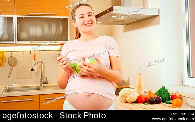 Happy smiling pregnant woman with big belly holding big bowl with fresh vegetable salad