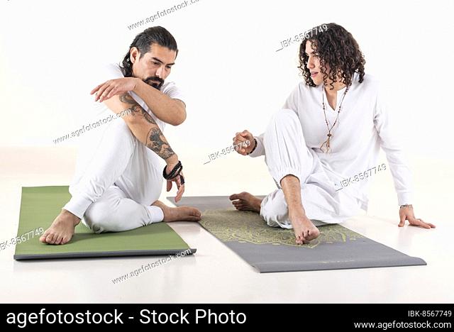 A yoga instructor is teaching yoga to a young man. Both dressed in white yoga clothes. Front view