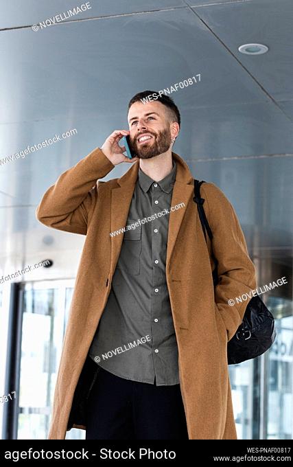 Male entrepreneur talking on mobile phone while standing with hands in pockets outdoors