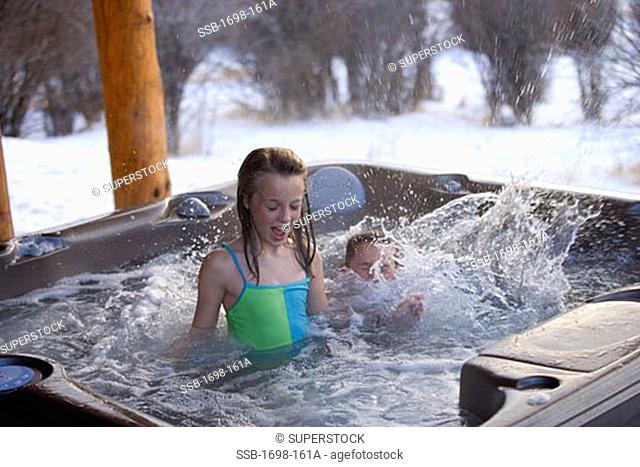 Girl in a hot tub with her brother splashing water