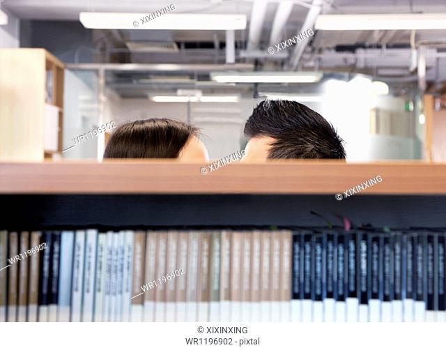 Work romance between two business people hiding behind shelves