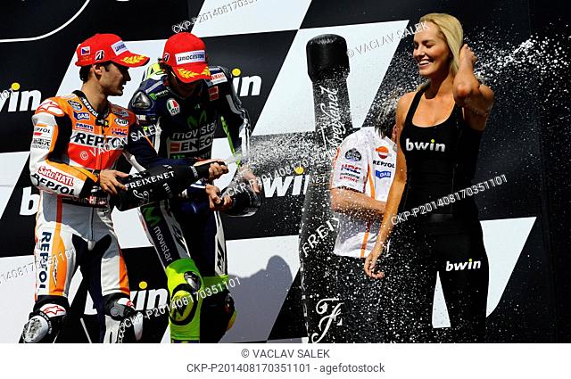 First placed Dani Pedrosa, of Spain, left, and third placed Valentino Rossi, of Italy, center, spray champagne on the hostess