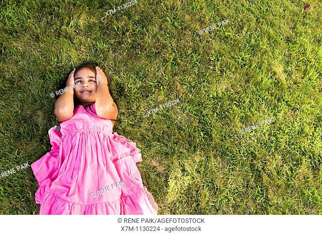 A little Indian girl thinking while laying on green grass