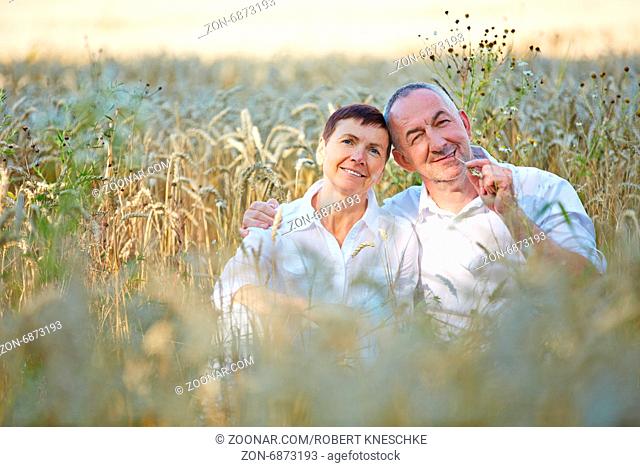 Glückliches Paar Senioren sitzt in einem Feld voller Weizen im Sommer