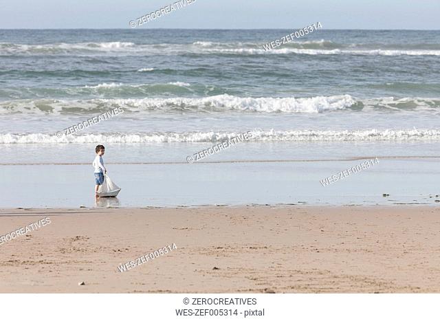 South Africa, Witsand, little boy playing with toy sailing boat on the beach
