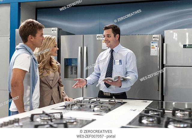 Shop assistant talking to young couple shopping kitchen equipment